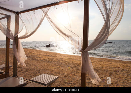 Schöne Aussicht auf einen Strand im Sonnenuntergang durch die Vorhänge eine Strandliege Stockfoto