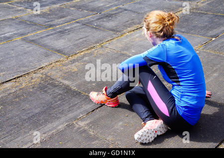 Eine Mädchen gekleidet als Sportler sitzt auf dem Boden in ein altes Stadion, warten auf sie an der Reihe. Stockfoto