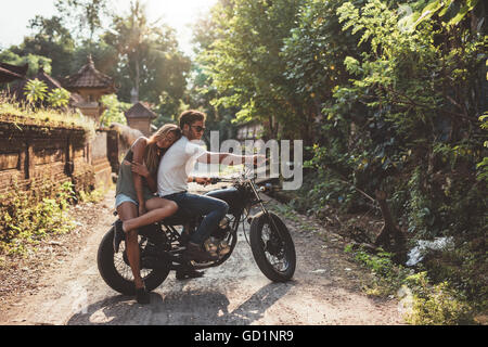 Junges Liebespaar auf einem Motorrad. Junger Mann und Frau auf dem Motorrad in einem Dorf an einem Sommertag. Stockfoto
