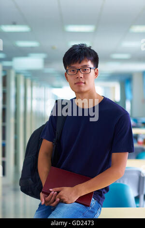 Eine junge männliche asiatische und chinesische Studenten Blick auf Kamera Lächeln in der Bibliothek Stockfoto