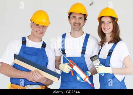 Drei lachende Arbeiter tragen Schutzhelme mit verschiedenen Werkzeugen Stockfoto