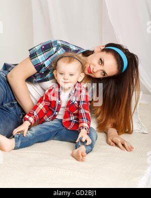 Mutter und Tochter zu Hause. Junge Mutter und Tochter umarmt. Mädchen in kariertes Hemd gekleidet. Tochter barfuß. Familie Stockfoto