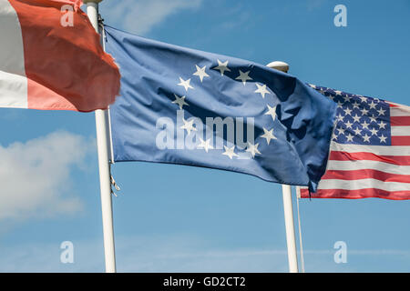 Französische, europäische und amerikanische Flaggen im Wind auf weißen Fahnenmasten mit blauen Himmel und flauschigen Wolken im Hintergrund wogenden Stockfoto