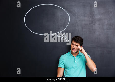 Verärgert unglücklich junger Mann stehen und Weinen über Blackboard-Hintergrund Stockfoto