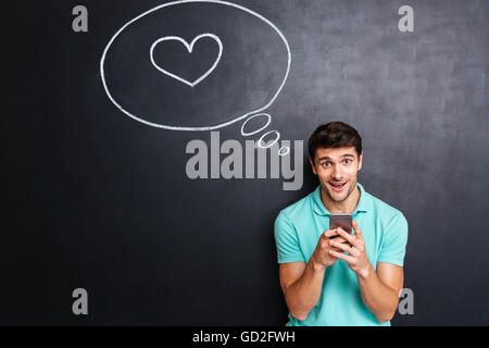 Lächelnde junge Mann in der Liebe mit Smartphone mit Herzen in der Sprechblase Stockfoto