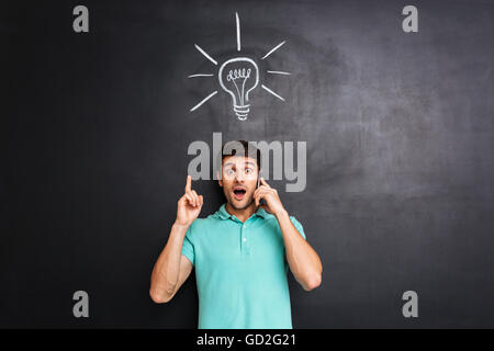 Jungen Mann am Handy sprechen und haben eine Idee über Blackboard Hintergrund erstaunt Stockfoto