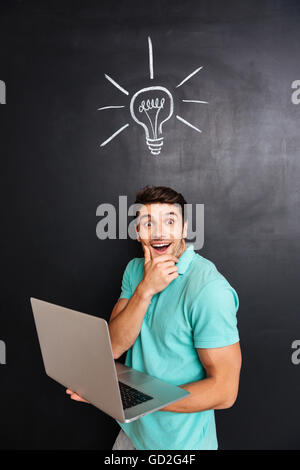 Überrascht, glücklich, junger Mann mit Laptop-Computer über Tafel Hintergrund Stockfoto