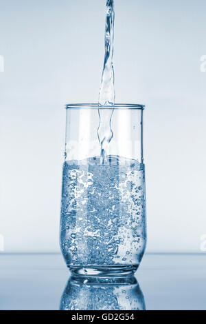 Wasser in ein Glas gießen, über blauem Hintergrund Stockfoto
