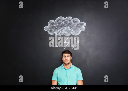 Überrascht, erstaunt junger Mann stehen unter Regenwolke mit Blitz und Regen auf Tafel Hintergrund gezeichnet Stockfoto