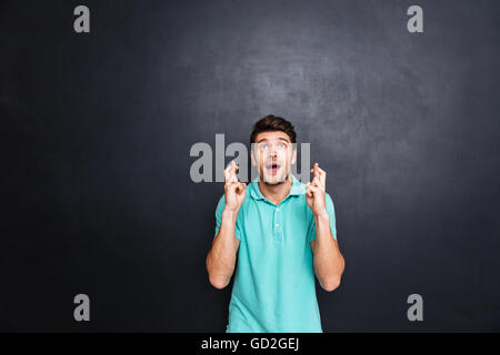 Hübscher junger Mann mit seinen Fingern gekreuzt schwarze Tafel, Glück Geste isoliert Stockfoto