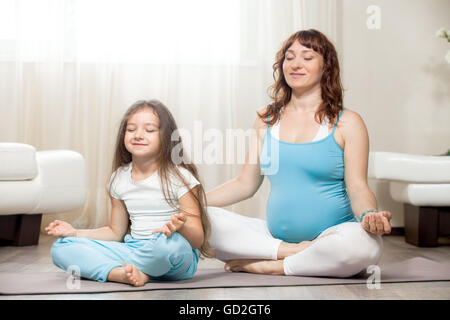 Familie gesunde Lifestyle-Konzept. Schwangerschaft-Yoga und Fitness. Junge glücklich schwanger Yoga Mutter ausruhen nach dem Training mit Kind Mädchen Stockfoto