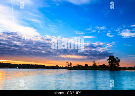 Sonnenaufgang über den türkisblauen See, Bäume und Wald am Horizont. Stockfoto