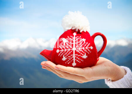 Teekanne in der geknoteten Kappe in der Hand einer Frau vor Bergkulisse Stockfoto