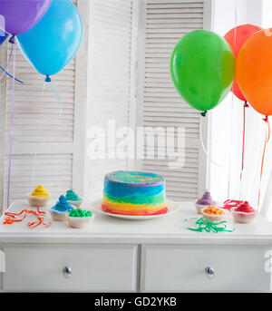 Regenbogen Kuchen und Cupcakes auf der Geburtstagsparty. Luftballons auf dem Hintergrund Stockfoto