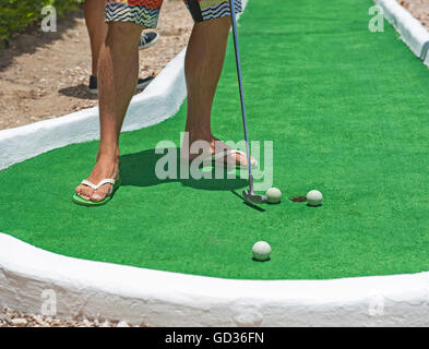 Mann in flip flop Sandalen im Sommerurlaub spielen Mini Golf Putting Kugel an der Bohrung Stockfoto