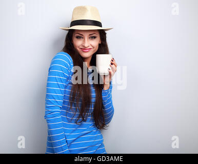 Süß glücklich casual Woman in Strohhut halten in der hand Tasse Tee und lächelnd auf blauem Hintergrund Stockfoto