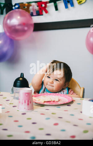 Ein Kind, ein einjähriges Mädchen auf ihrer Geburtstagsparty, in einen Hochstuhl an einem Tisch sitzen. Stockfoto