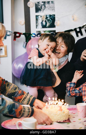 Eine Familie versammelt, um ein einjähriges Mädchen-Geburtstags-Party zu feiern. Ein Kuchen mit vielen Kerzen. Stockfoto