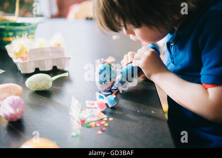 Ein Kind, Verzierung von Eiern zu Ostern mit Glitzer, Leim und Lack. Stockfoto