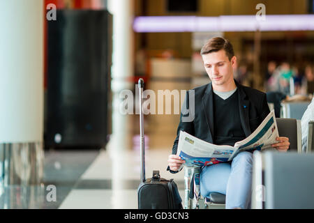 Kaukasischen Jüngling mit Zeitung am Flughafen beim Boarding warten. Lässige jungen Geschäftsmann tragen Jackett. Stockfoto