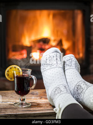 Wärmend und entspannend in der Nähe von Kamin. Frau Füße in der Nähe von der Tasse Glühwein am Kamin. Stockfoto