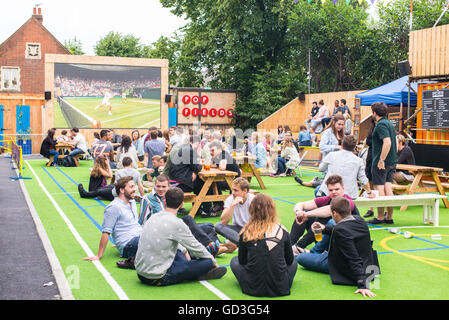 Die Menschen reden und trinken während Sie Wimbledon Tennis Match in einem großen draußenen Bildschirm in pop Felder, brixton Stockfoto