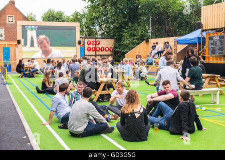 Die Menschen reden und trinken während Sie Wimbledon Tennis Match in einem großen draußenen Bildschirm in pop Felder, brixton Stockfoto