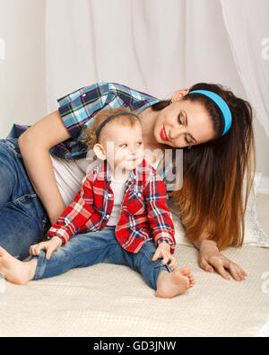 Mutter und Tochter zu Hause. Junge Mutter und Tochter umarmt. Mädchen in kariertes Hemd gekleidet. Tochter barfuß. Familie Stockfoto