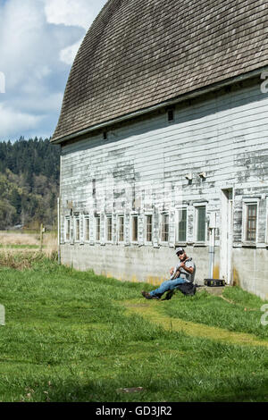 Man spielt ein Banjo neben einer alten Scheune in Nisqually National Wildlife Refuge, Nisqually, Washington, USA Stockfoto