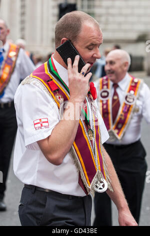 Belfast, UK. 12. Juli 2016. Ein Mann auf seinem Handy nach der Prozession von Demonstranten gestoppt während der 12. März. Es entstand während des späten 18. Jahrhunderts in Ulster. Es feiert die Glorious Revolution (1688) und der Sieg des protestantischen Königs Wilhelm von Oranien über katholische König James II an Schlacht des Boyne (1690) Credit: Bonzo/Alamy Live News Stockfoto