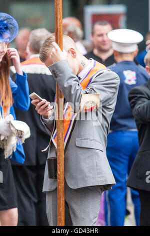 Belfast, UK. 12. Juli 2016. Ein Mann, der sein Handy überprüfen, nachdem der Zug der Demonstranten während der zwölften März beendet. Es entstand während des späten 18. Jahrhunderts in Ulster. Es feiert die Glorious Revolution (1688) und der Sieg des protestantischen Königs Wilhelm von Oranien über katholische König James II an Schlacht des Boyne (1690) Credit: Bonzo/Alamy Live News Stockfoto