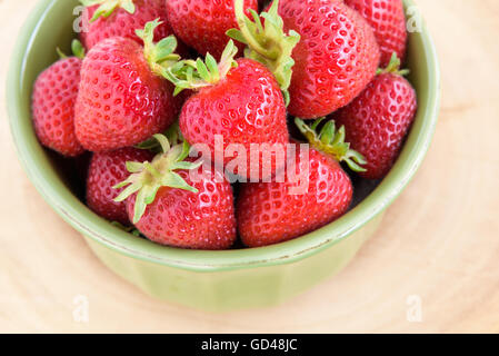 Frisch gepflückte Erdbeeren in einer grünen Schale auf einer hölzernen Platte Stockfoto