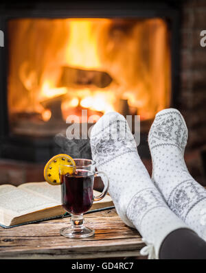 Wärmend und entspannend in der Nähe von Kamin. Frau Füße in der Nähe der Tasse heiß und ein Buch Wein am Kamin. Stockfoto