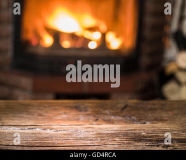 Alten Holztisch und Kamin mit warmen Feuer im Hintergrund. Stockfoto