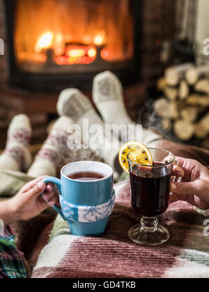 Wärmend und entspannend in der Nähe von Kamin. Frau Füße in der Nähe von der Tasse heißes Getränk am Kamin. Stockfoto