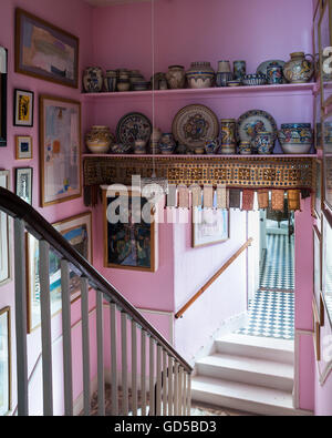 Sammlung von Poole Tonwaren in Regalen in rosa Treppenhaus mit verschiedenen Kunstwerken an Wänden Stockfoto