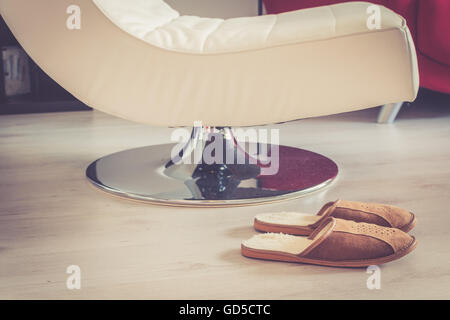 Brauner Wolle bequeme Hausschuhe vor Lounge Stuhl auf grauen Holzboden im Wohnzimmer Stockfoto