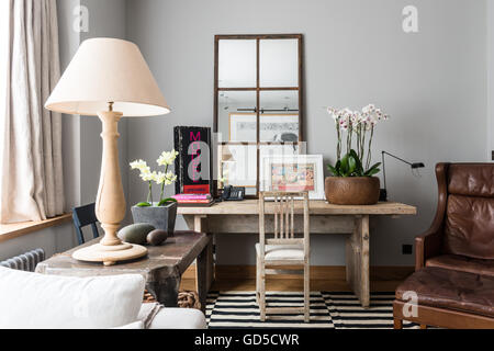 Holz-Topf mit Orchideen auf rustikalen Holztisch im Wohnzimmer mit holzverkleideten Spiegel und Flügel zurück Ledersessel Stockfoto