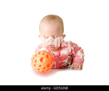 Kleine Mädchen tragen weiße und rosa Pyjama, rote Socken spielt mit ihren orange Ball liegend auf dem Bauch Stockfoto