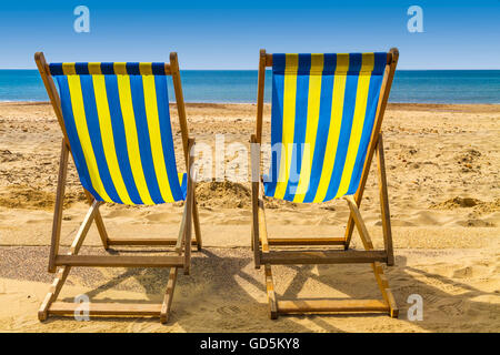 Zwei blaue und gelbe Liegestühlen mit Blick aufs Meer über goldenen Sand an einem sonnigen Tag, Bournemouth, UK Stockfoto