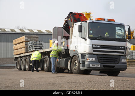 Ein LKW-Fahrer passt die Steuerung des Krans Fahrerhaus montiert, während den Anhänger in einem Gebäude laden Produkte Hof Stockfoto