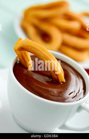 Churros con Chocolate, eine typisch spanische süße Jause, auf einem blauen rustikalen Holztisch Stockfoto