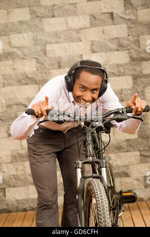 Mann trägt graue Büro Hosen, weiße rote Businesshemd mit dem Fahrrad im Rennsport Position lächelnd, Ziegel Wand Hintergrund stehend Stockfoto
