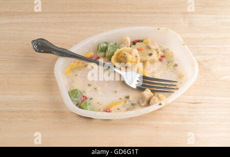 Ein Huhn mit Tortellini und Gemüse TV Dinner fast fertig in der Plastikschale mit einer Gabel auf einem Holztisch. Stockfoto