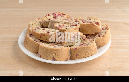 Mehreren Cranberry-Mandel-Biscotti eingetaucht in weißer Schokolade auf einem weißen Teller oben auf einem Holztisch. Stockfoto