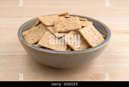 Eine alte Steingut-Schale gefüllt mit Bio Vollkorn Cracker auf einem Holztisch. Stockfoto