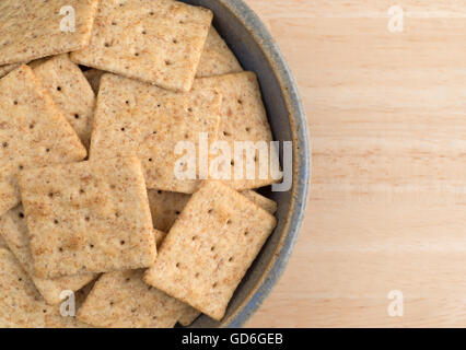 Enge Draufsicht eine alte Steingut-Schale gefüllt mit Bio Vollkorn Cracker auf einem Holztisch. Stockfoto