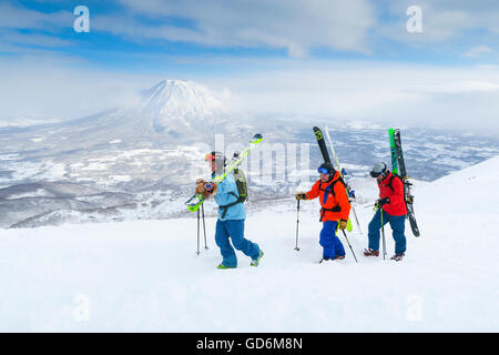 Eine weibliche und zwei männliche Backcountry Skifahrer Wandern mit dem Vulkan Yotei im Hintergrund auf den Gipfel des Mount Annupuri, im Skigebiet Niseko United auf der japanischen Insel Hokkaido.     Niseko United besteht aus vier Resorts auf ein mou Stockfoto