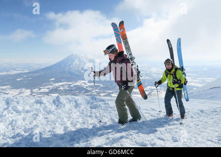 Mit dem Vulkan Yotei im Hintergrund sind weibliche und männliche Backcountry Skifahrer auf den Gipfel des Mount Annupuri, in der Nähe von Skigebiet Niseko United auf der japanischen Insel Hokkaido wandern.     Die Skier, die sie tragen auf ihren Rucksack sind groß und breit ermöglicht Stockfoto