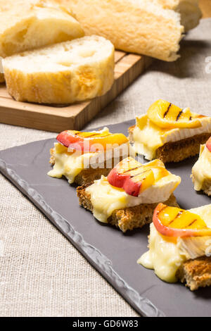 Kanapees, Vorspeise mit gegrilltem Brie und Nektarine auf einer Schiefertafel Schale vergoldet Stockfoto